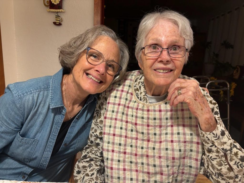 Two older women wearing glasses smiling together during a visit.